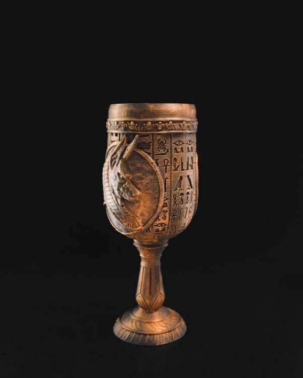 Ancient Egyptian goblet with hieroglyphs and reliefs of Anubis on a black background.
